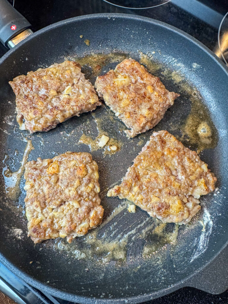 Four poor man's steaks browning in a skillet with melted butter.