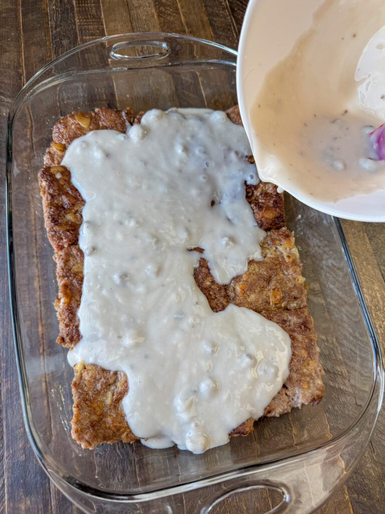 Mixing bowl pouring mushroom gravy over top of poor mans steak.
