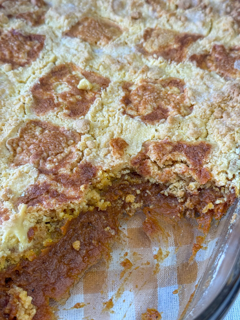 A couple scoops of warm, spice flavored pumpkin filling under a layer of buttery bake yellow cake in a glass dish.