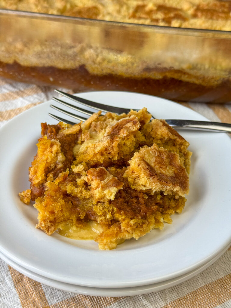 Pumpkin pie filling with aromatic spices and a classic white cake mix layer baked on top with plenty of butter and the full cake in the background.