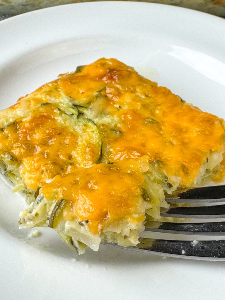 Fork lifting a bit of rich and delicious cheesy zucchini casserole off of a plate.