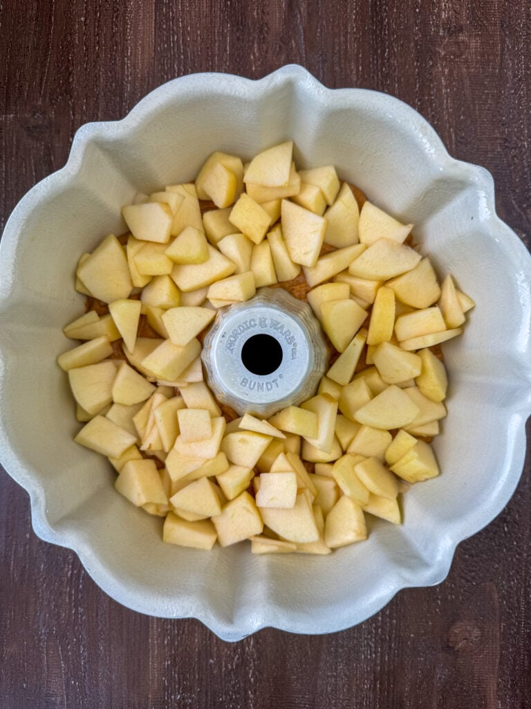 Chopped apples layered on pumpkin spice cake batter in a bundt cake pan.