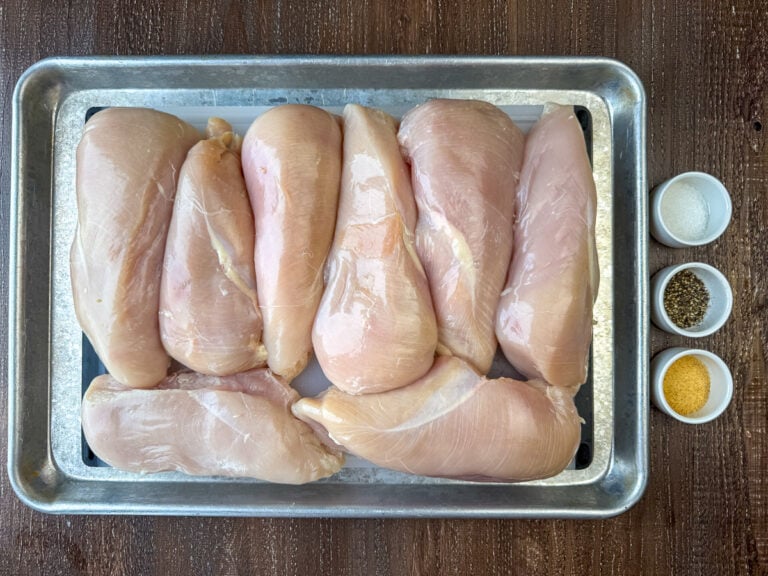 Ingredients to make shredded chicken are chicken breasts, salt, pepper and granulated garlic on a wooden counter top.
