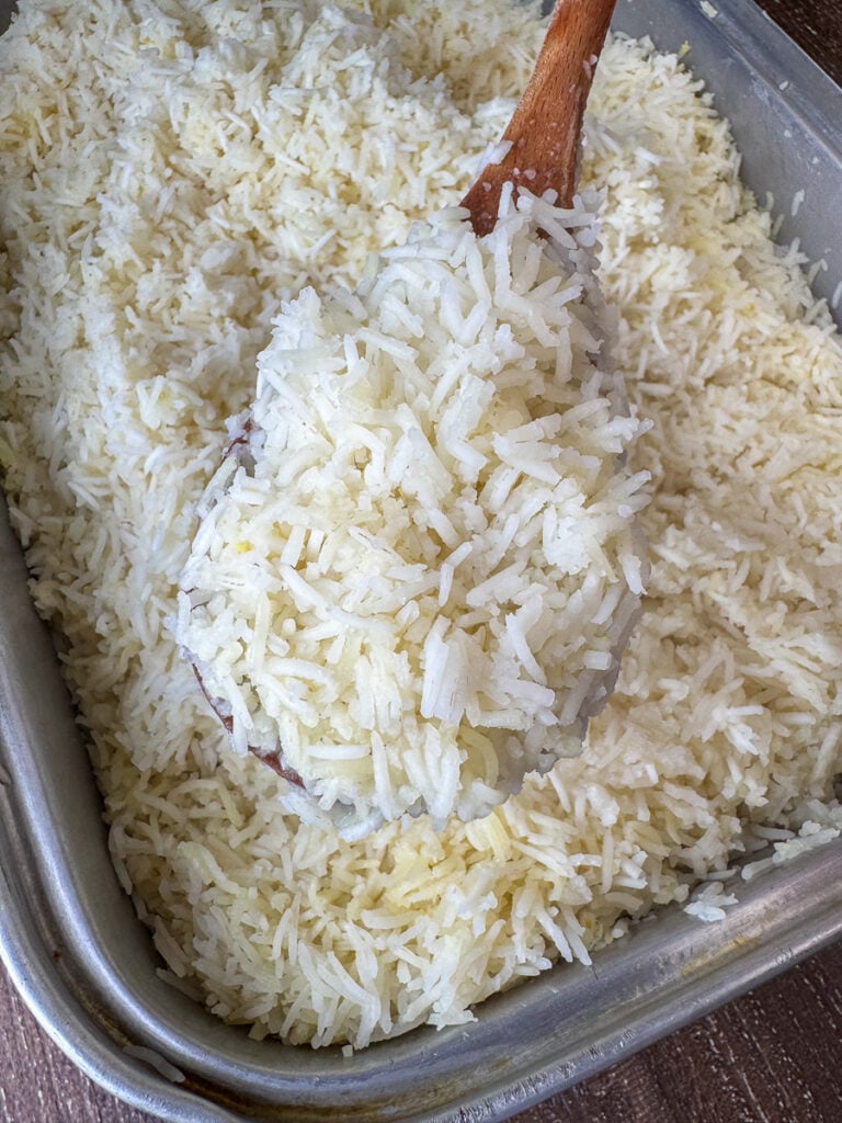Close up of a spoon full of rice being lifted above a big roaster of warm rice for a crowd.