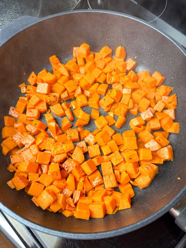 Small cubes of sweet potatoes frying in sausage drippings in a non-stick skillet pan.