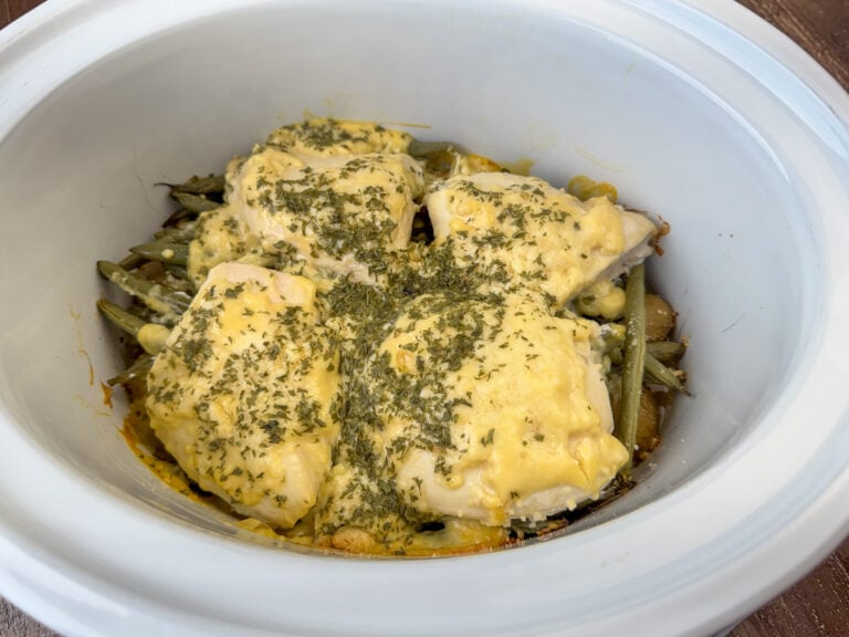 Side view of tender and delicious crock pot full of chicken breasts with a creamy parmesan topping and cooked on potatoes and green beans.