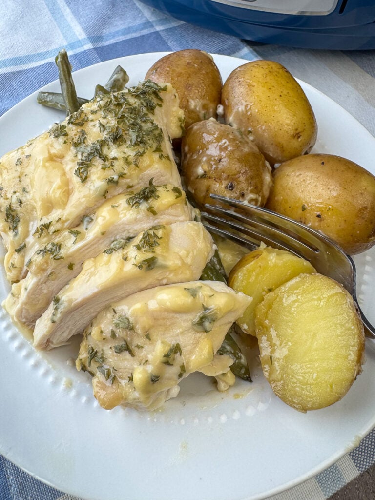 Overhead view of a plate full of sliced chicken with a creamy parmesan topping next to baby potatoes with a fork ready to take a bite.