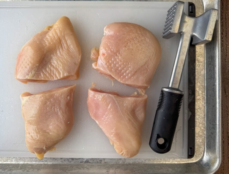 Two chicken breasts pounded to level out and cut in half on a cutting board.