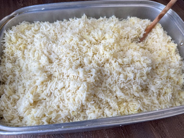 Wooden spoon fluffing up a warm batch of oven baked rice for a crowd in a big silver roaster.