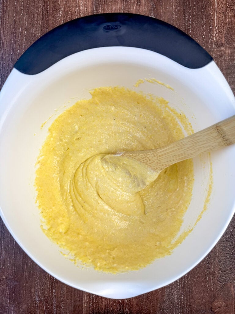 Wooden spoon stirring together Jiffy corn muffin batter.