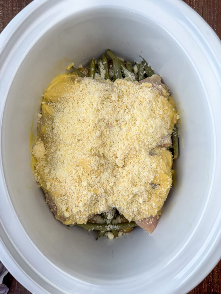 Grated parmesan cheese sprinkled over chicken coated with garlic and cream of chicken soup in a white crock.