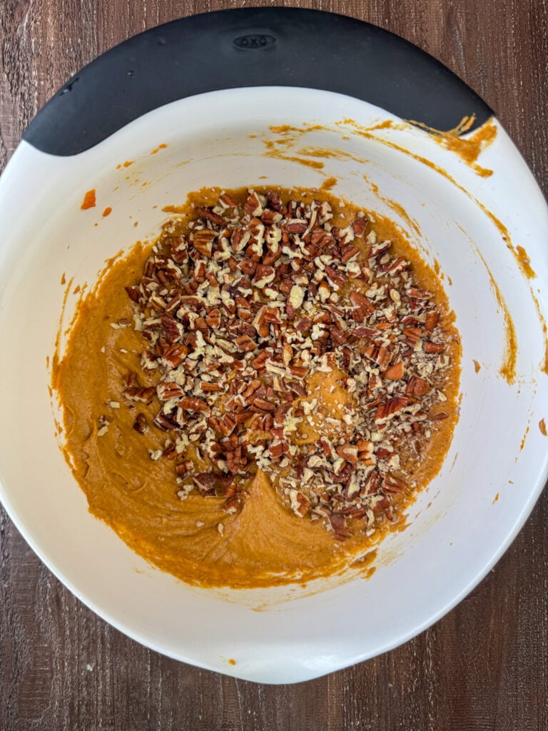 Pecans sprinkled over a bowl of pumpkin spice cake batter.