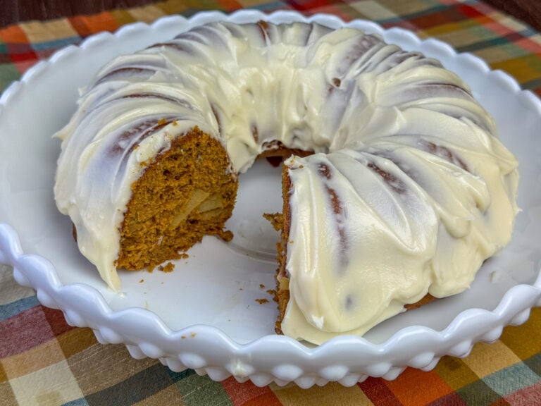 Side view of a warm and delicious pumpkin apple spice cake coated with frosting on a beautiful white dish.