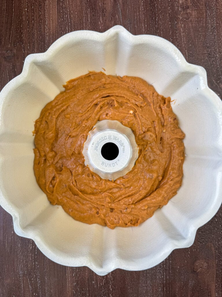 A portion of the pumpkin spice batter recipe spread in the bottom of a bundt pan on a wooden counter.