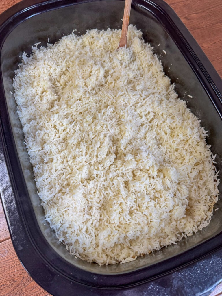 Overhead view of an electric roaster with a big batch of Basmati long grain rice with a wooden spoon ready to serve.