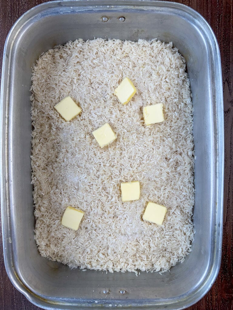 Salt and slices of butter spread over 5 pounds of rinsed rice in a large roaster pan.