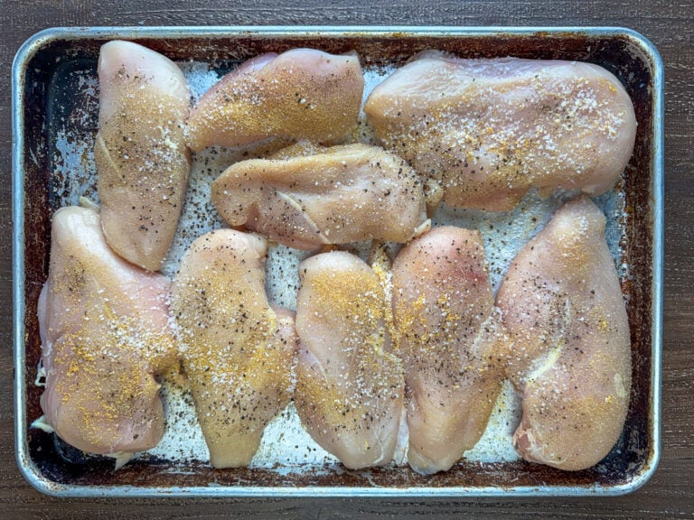 Overhead view of 5 pounds of lightly seasoned boneless skinless chicken breasts on a baking sheet.
