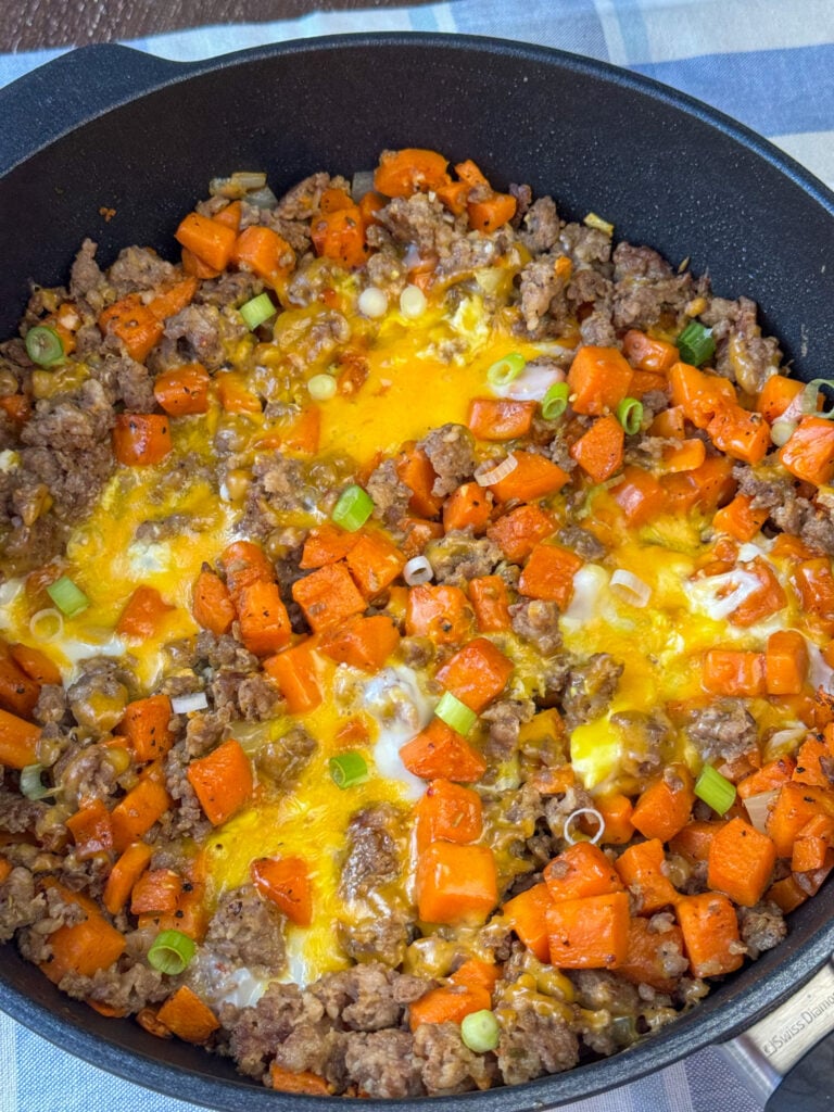 Overhead view of a sausage and sweet potato breakfast hash in a one skillet meal with cheese and green onion slices on top.