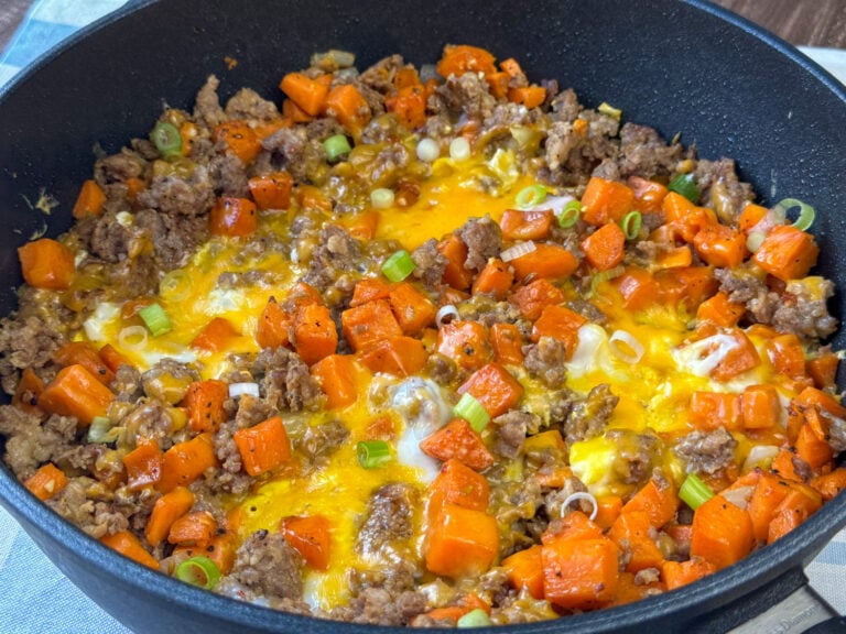 Side view of crumbled Italian sausage nestled in tender sweet potato cubes with a few eggs added and cheddar cheese on top.