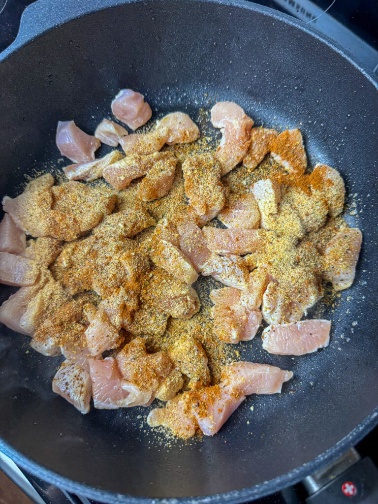 Cubes of raw chicken seasoned with garlic powder, paprika, salt and pepper in a non-stick skillet.