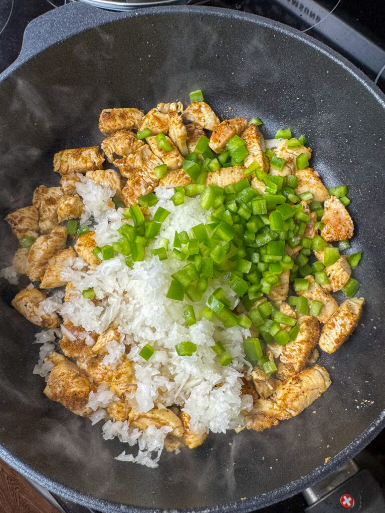 Cooked chunks of chicken with raw rice and chopped green pepper added on top.