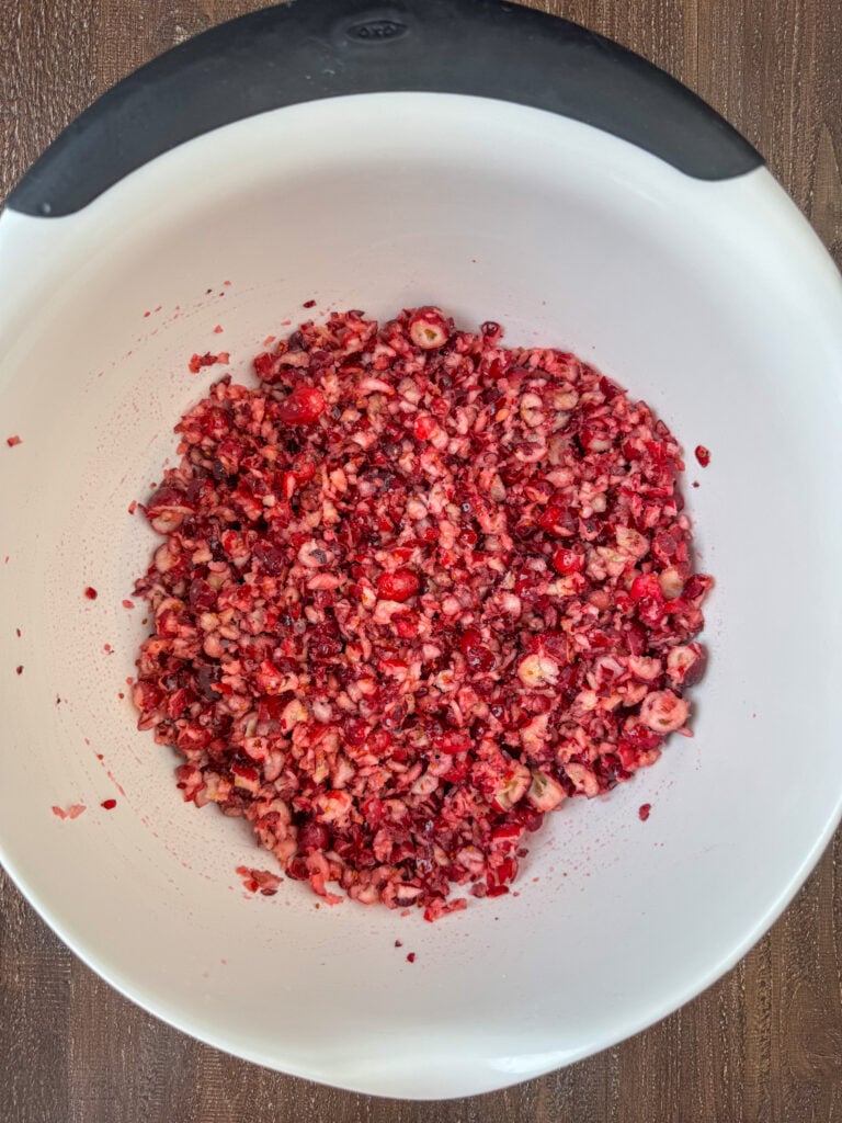 Chopped cranberries in a mixing bowl with sugar stirred in.