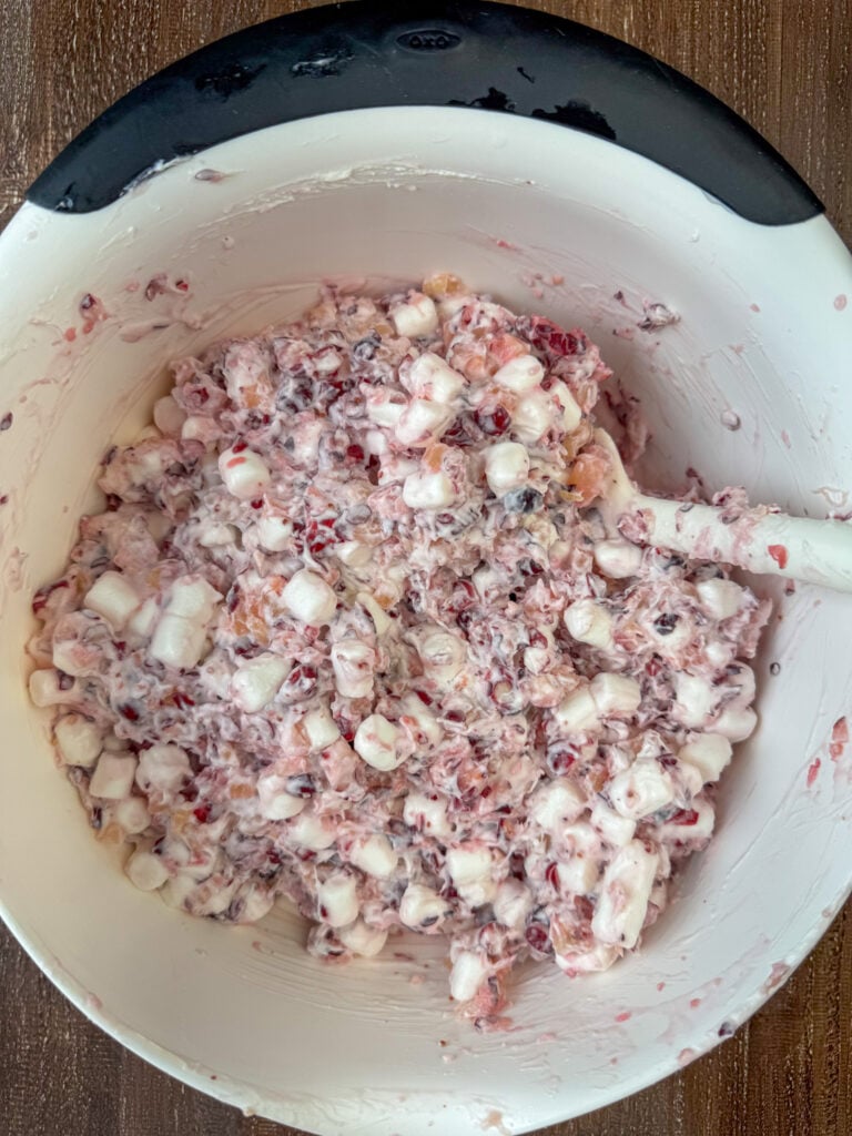 Spatula stiffing whipped cream and marshmallows into a sweet cranberry fluff recipe.