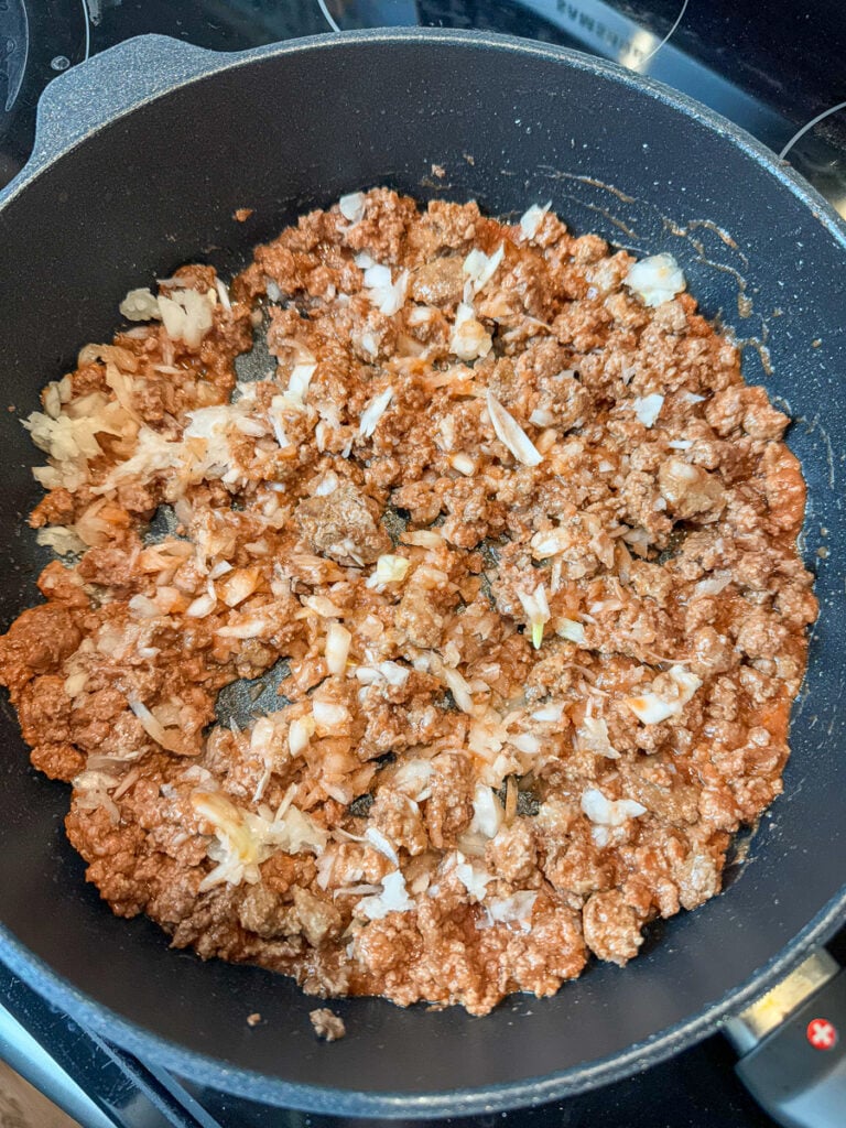 Ground beef cooking with chopped onions and tomato sauce in a non-stick skillet.