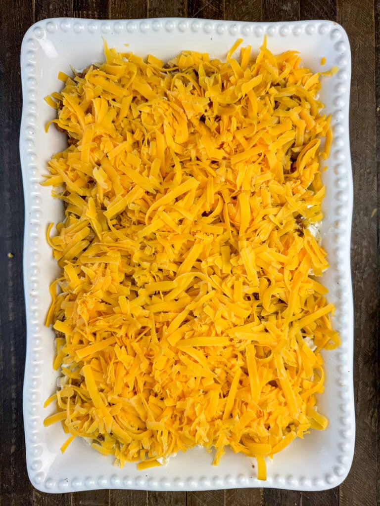 Layer of thick cheddar cheese spread over an old fashioned sour cream noodle bake in a casserole dish.