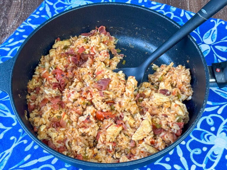 Side view of flavorful chicken and rice that cooked in one pot with bacon and fire roasted tomatoes and a spoon ready to lift a scoop out.