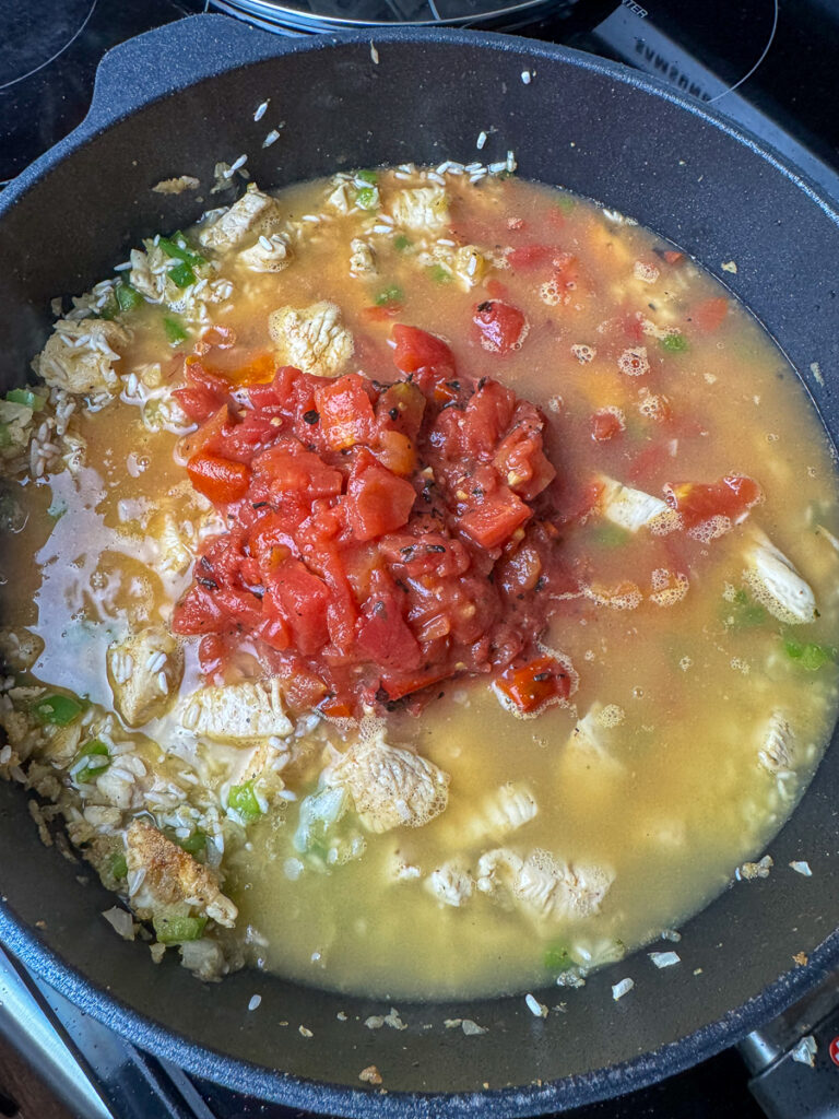 Chicken broth and fire roasted tomatoes added to a deep skillet of chicken and rice.
