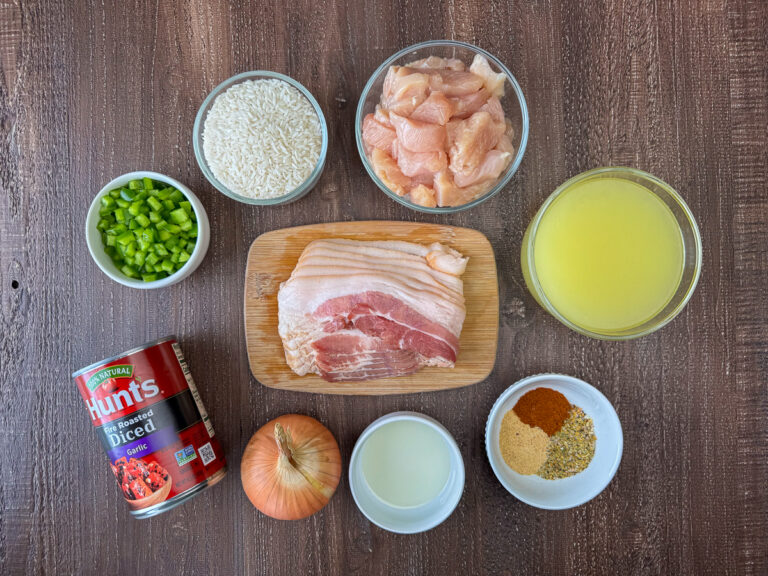 Ingredients to make one skillet chicken and rice are raw white rice, chicken breast, chicken broth, bacon, green pepper, fire roasted tomatoes, onion, vegetable oil, garlic powder, paprika, salt and pepper on a wooden counter top.