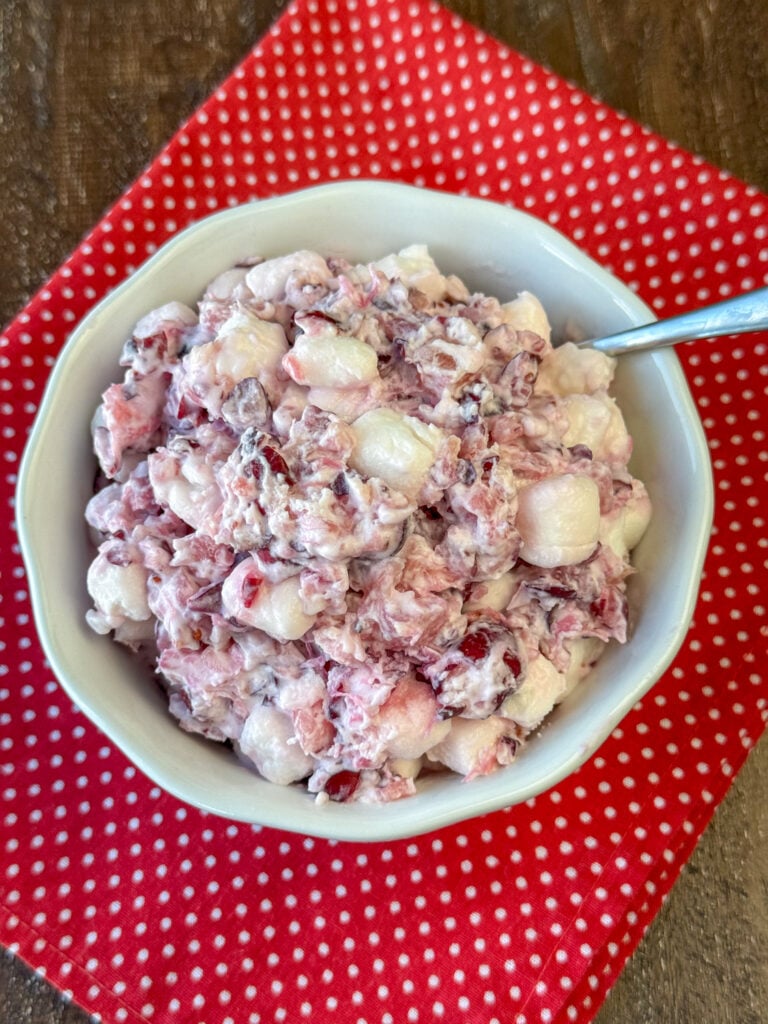 Overhead view of bowl of Cranberry Pineapple Fluff on a red and white napkin on a wooden counter top.