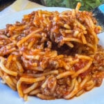 Close up pieces of spaghetti in a generous meat sauce with a fork ready to take a bite.
